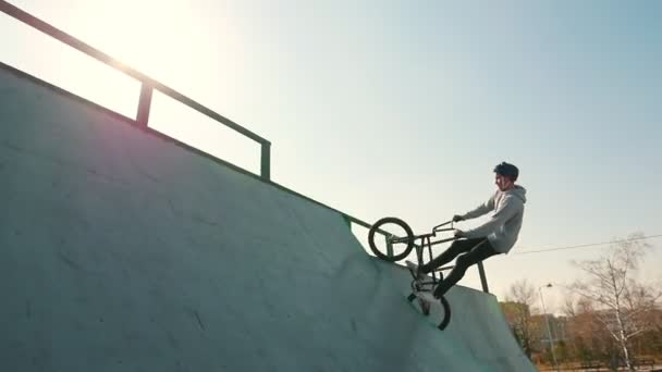 Un BMX coureurs de formation de leurs compétences dans le skatepark. Course vers le haut, effectuant un flip et descendant sur un fond lumineux de soleil — Video