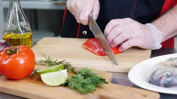 A chef in the kitchen cutting a red pepper