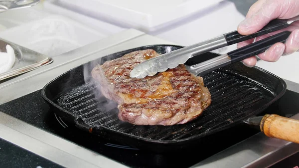 レストランのキッチンで働くシェフ。フライパンでステーキを炒める。肉をひっくり返すシェフ — ストック写真