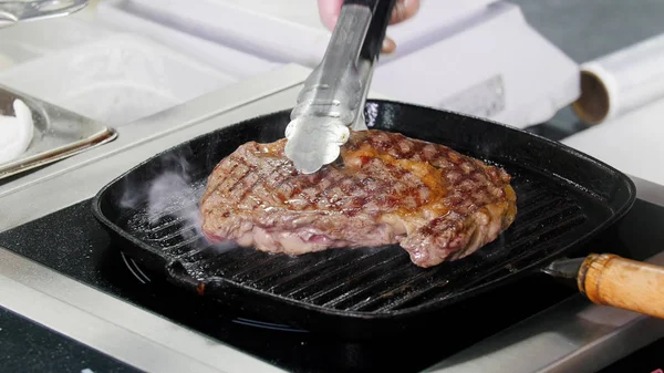 レストランのキッチン。フライパンでステーキを炒める。肉をひっくり返すシェフ — ストック写真