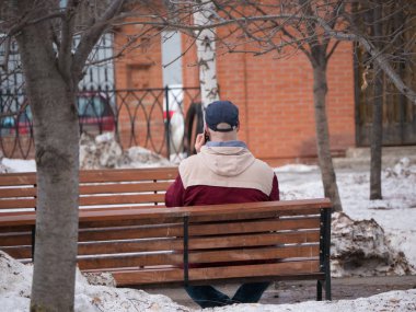 Şehir sokakları. Bankta oturan ve telefonuyla konuşan bir adam.