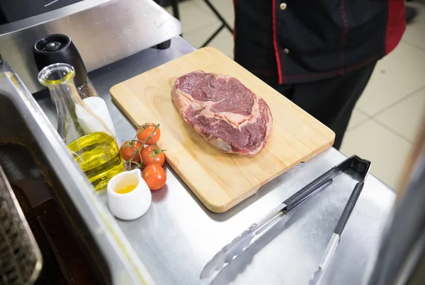 Uno chef che lavora in cucina. Pezzo di carne crudo sul tavolo — Foto Stock