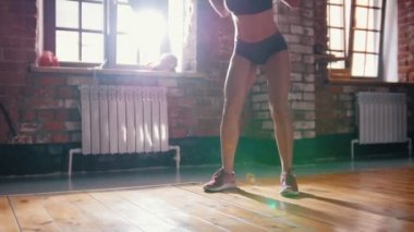 Spor salonunda eğitim alan bir kadın. Arkasında bir dambılile çömelmek