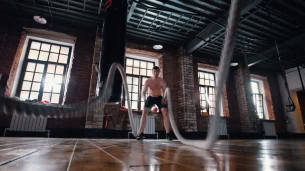 Een atletische man op training in de sportschool. Trainen van zijn handen met touwen raken — Stockvideo