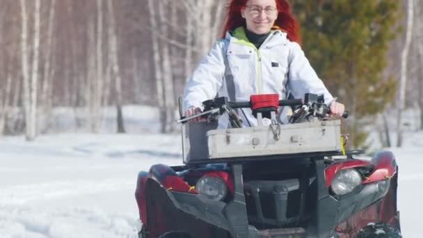 Una mujer sonriente con pelo de jengibre montando moto de nieve en el bosque — Vídeos de Stock