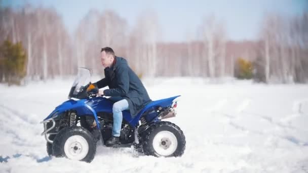 Un bosque de invierno a la luz del día. Un hombre montando una gran moto de nieve azul — Vídeos de Stock