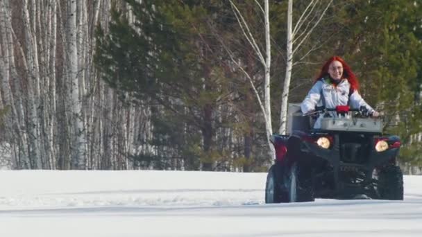 Un bosque de invierno. Una mujer con el pelo de jengibre cabalgando gran moto de nieve roja — Vídeo de stock