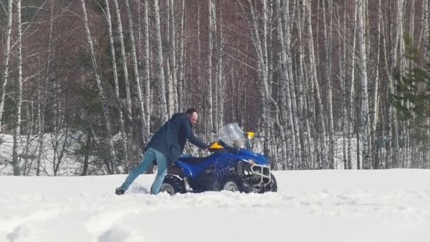 Uma floresta de inverno. Um homem tenta tirar a mota de neve da neve. — Vídeo de Stock