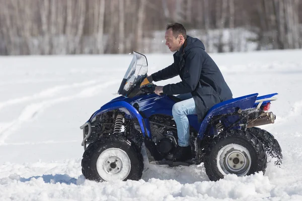 Un bosque de invierno a la luz del día. Un hombre montando una gran moto de nieve azul — Foto de Stock