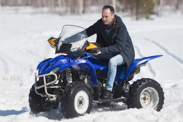 Un bosque de invierno a la luz del día. Clima frío. Un hombre adulto montando una gran moto de nieve azul — Foto de Stock