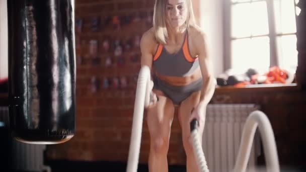 Een atletische vrouw op training in de sportschool. Trainen van haar handen met touwen raken — Stockvideo