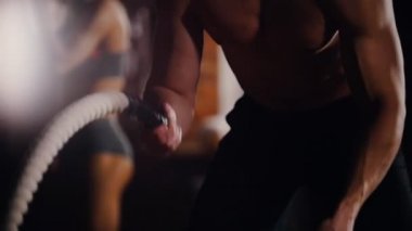 Crossfit. Spor salonunda antrenman. Ellerini halatlarla eğiten bir adam yere vuruyor ve bir arka plandaki kadın egzersizyapıyor.