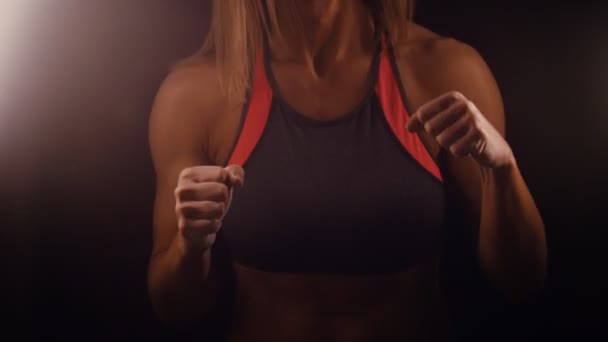 Una mujer atlética de pie en la oscuridad y realizando una pelea con una sombra — Vídeos de Stock