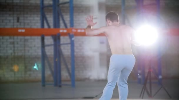 A bright room. An athletic shirtless man training his capoeira skills — Stock Video