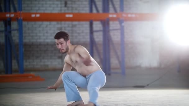 Una habitación luminosa. Un hombre atlético sin camisa entrenando sus habilidades de capoeira y saltando sobre sus manos — Vídeo de stock