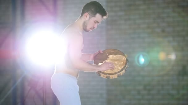En man som spelar tamburin i ett ljust rum — Stockvideo