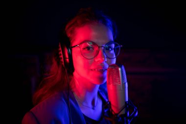 Neon ışıkta mikrofontarafından şarkı söyleyen ve kameraya bakan gözlüklü genç bir kadın