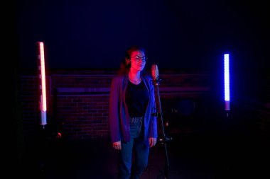 Backstage. Neon Aydınlatma mikrofonun yanında duran gözlüklü genç bir kadın