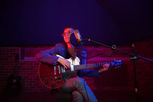 A young woman in glasses playing guitar and singing in neon lighting — Stock Photo, Image