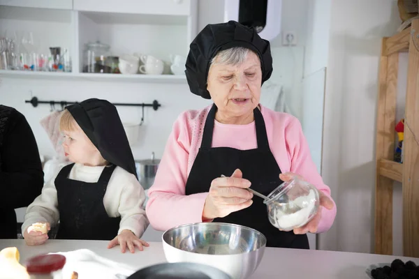 La familia hace panqueques. Una anciana poniendo la pasta en la sartén —  Fotos de Stock