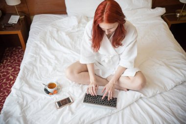 Otel odasında yatakta oturan ve bir dizüstü bilgisayar ile çalışan bir zencefil kadın