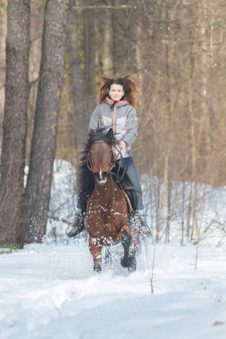 Sıcak ceketli bir kadın kahverengi bir ata biniyor.