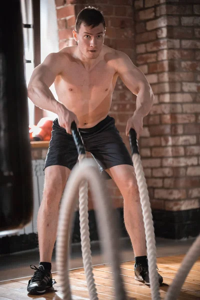 Crossfit. Um homem concentrado no treino no ginásio. Treinando suas mãos com cordas batendo no chão — Fotografia de Stock