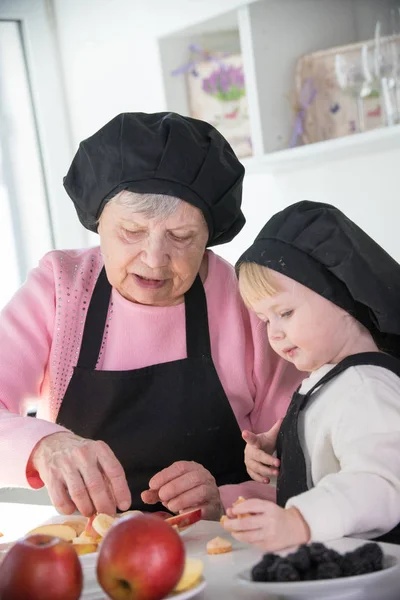 Küçük bir kız mutfakta bir porsiyon için meyve hazırlanıyor duran yaşlı bir kadın Telifsiz Stok Fotoğraflar