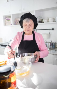Mutfakta krep yapan yaşlı bir kadın. Kasede hamur yapma