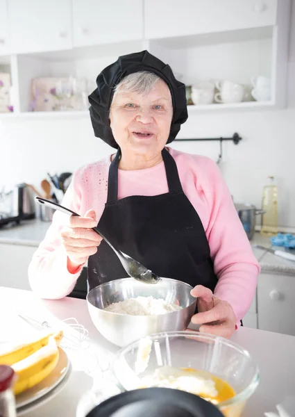 Счастливая старая женщина делает блинчики на кухне — стоковое фото