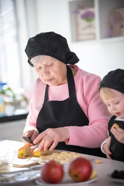 An old woman cutting an apple with a little girl in the kitchen