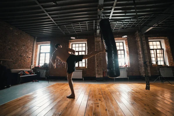 Un boxeador atlético entrenando con un saco de boxeo en el gimnasio. Patear la bolsa con una pierna — Foto de Stock