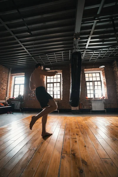 Spor salonunda kum torbası yla atletik bir boksör antrenmanı. Adam bir bacak ile çanta tekme hakkında — Stok fotoğraf