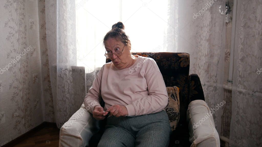 An old angry woman in glasses sitting in the armchair and knitting