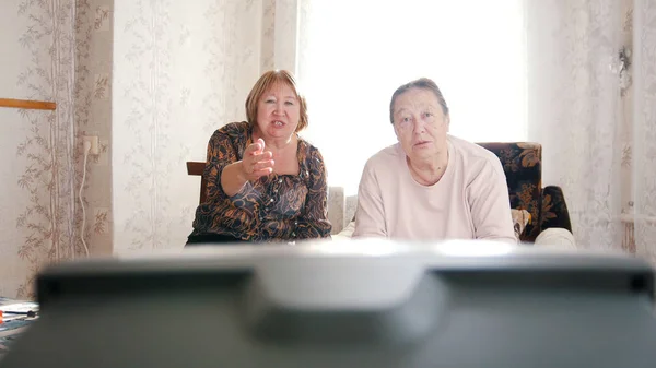 Mulheres idosas sentadas nas poltronas e assistem TV — Fotografia de Stock