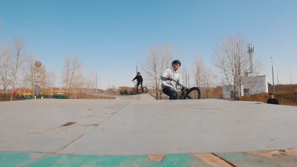 Ένας ποδηλάτης με γκρι φούτερ με κουκούλα που ιππεύει στο πάρκο του σκέιτμπορντ — Αρχείο Βίντεο