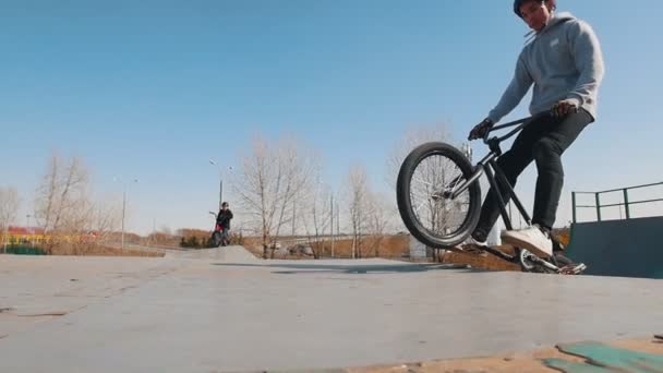 Un cavaliere bmx in felpa grigia cavalcando nello skatepark e manovelle il volante — Video Stock