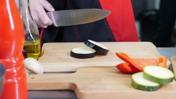 Um chef a trabalhar na cozinha. Cortar uma berinjela e uma cenoura — Vídeo de Stock