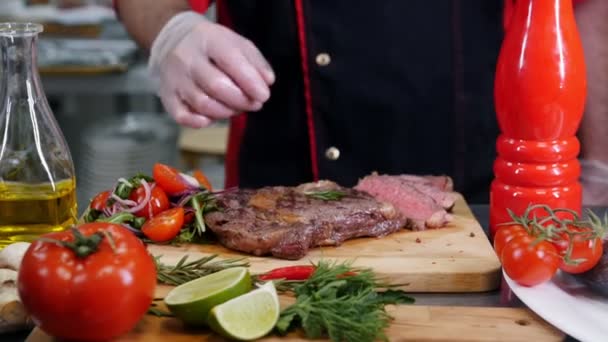 Ein Koch in der Küche. ein Mann serviert ein Steak mit Chilischote und nimmt das Gericht weg — Stockvideo