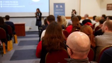 Bir iş konferansı. Sandalyelerde oturan ve salondaki sunum ekranına bakan insanlar