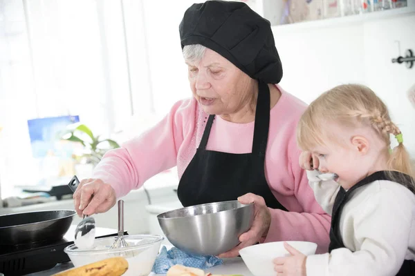 Familia en la cocina. Una abuela sosteniendo un tazón y un batidor — Foto de Stock