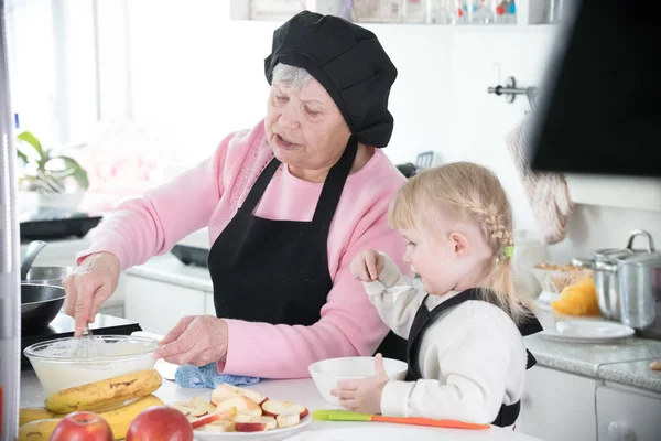 Familia en la cocina. Una abuela haciendo una pasta para panqueques — Foto de Stock