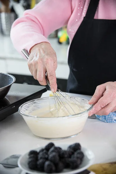 Домашняя кухня. Старуха делает тесто для блинчиков с помощью венчика. — стоковое фото