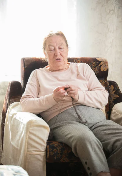 Une vieille femme assise dans le fauteuil et tricot — Photo