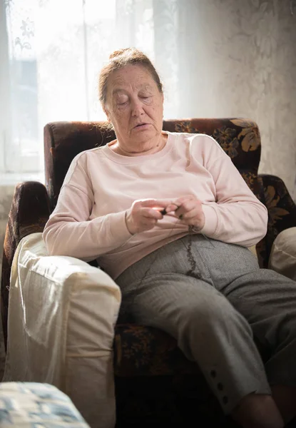 En gammal kvinna i tröjan sitter i fåtöljen och stickning — Stockfoto