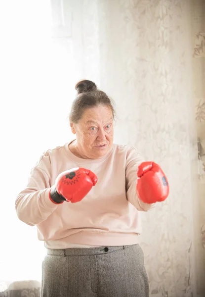 An angry old woman in red boxing gloves is ready to fight