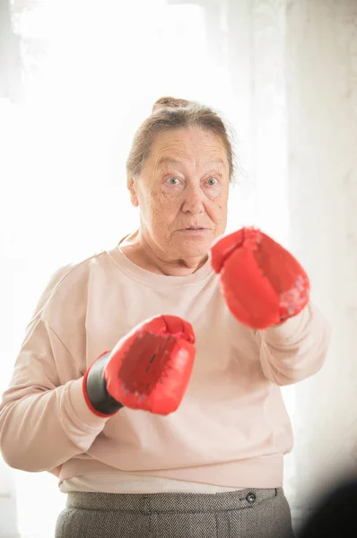 An old woman in sweater and boxing gloves is ready to fight