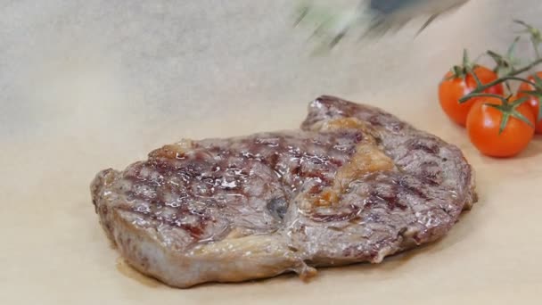 Restaurant keuken. Een chef-kok serveert een biefstuk in het papier met groen en cherry tomaten — Stockvideo