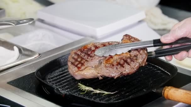Pracuju v kuchyni. Šéf drží steak nad pánví v kuchyňských kleštích — Stock video