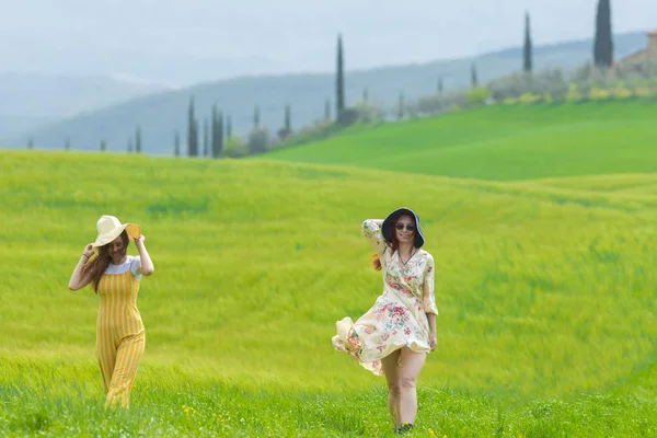 Due donne in cappelli luminosi che camminano su un prato verde brillante — Foto Stock